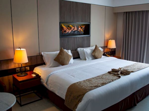 The image shows a neatly made hotel room bed with white linens and brown cushions, flanked by two bedside lamps on wooden nightstands, ending the sentence.
