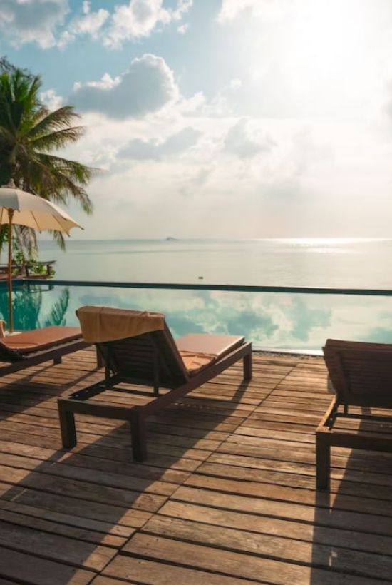 A serene poolside scene with lounge chairs, umbrellas, and a tranquil ocean view under a partly cloudy sky completes the picturesque setting.