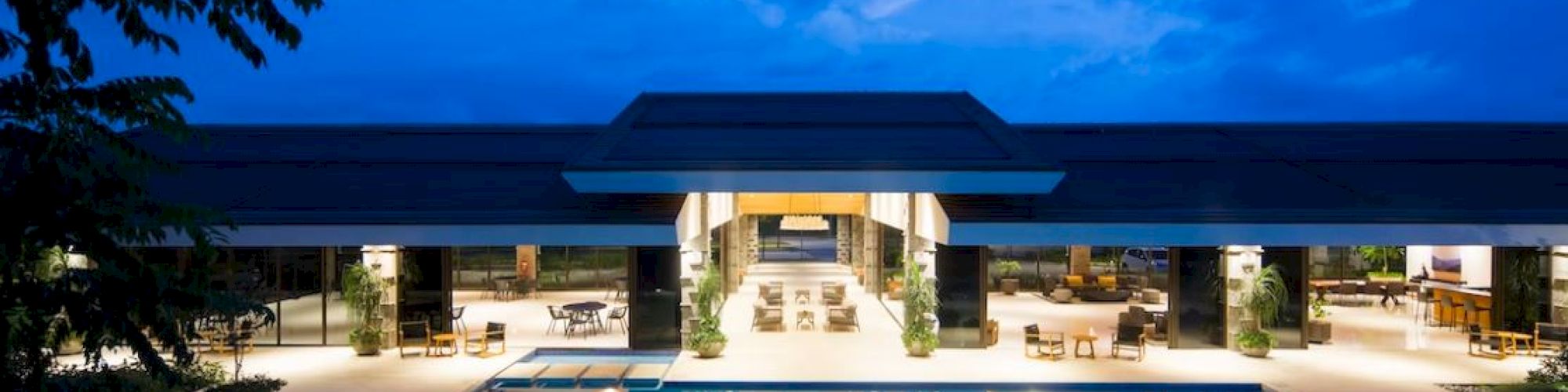 An elegant pool area with lounge chairs and a modern building in the background, all set against a twilight sky.