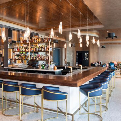 A modern bar with high chairs, a well-stocked liquor shelf, elegant lighting fixtures, and a lounge area with additional seating.