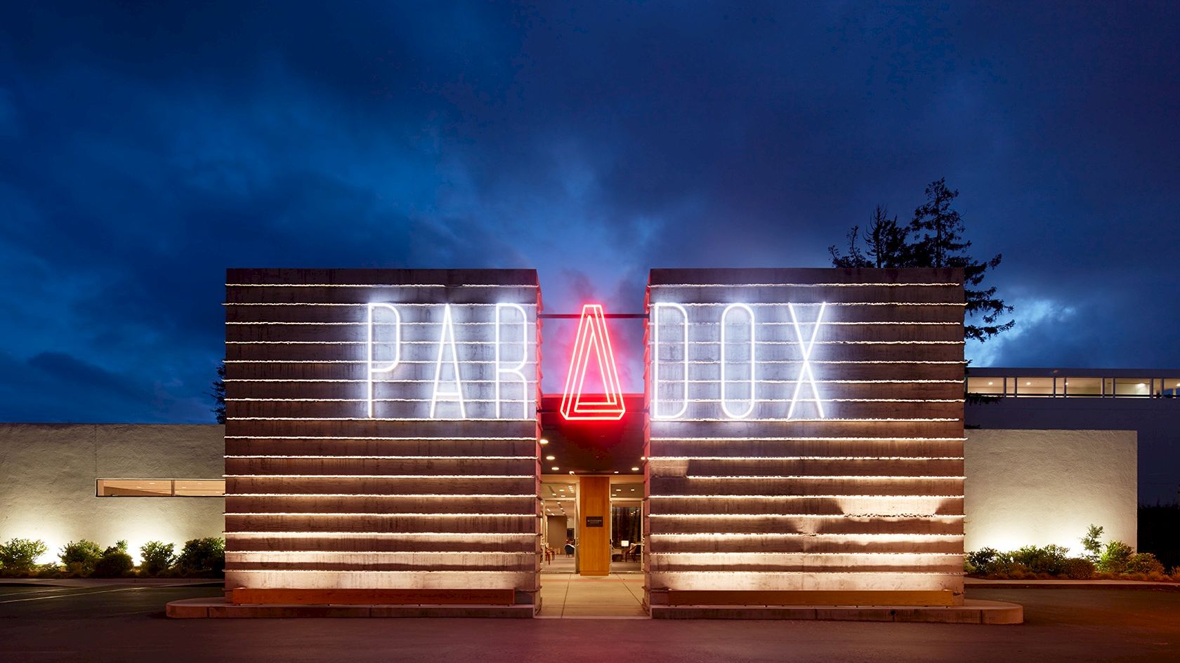 The image shows a modern building with a neon sign that reads "PARADOX" at night, with a distinct luminous triangle in place of the "A".