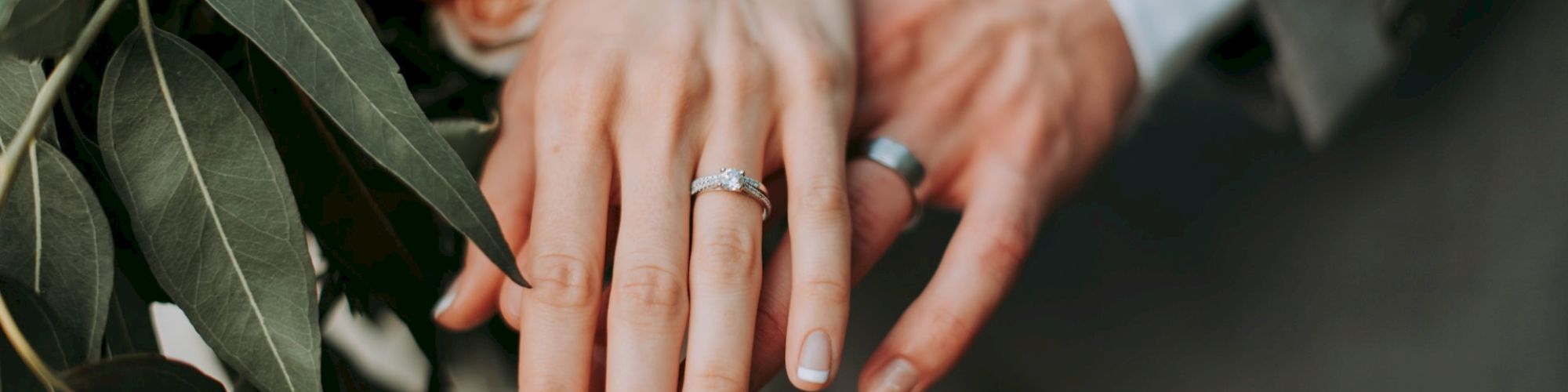 A close-up of two hands showing wedding rings, with a bouquet of flowers featuring red and orange roses in the background.