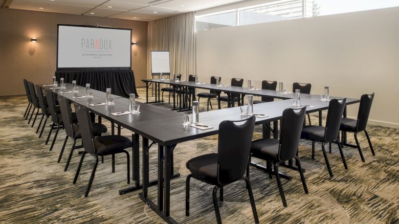 A conference room with U-shaped table setup, empty chairs, water glasses, a screen with 