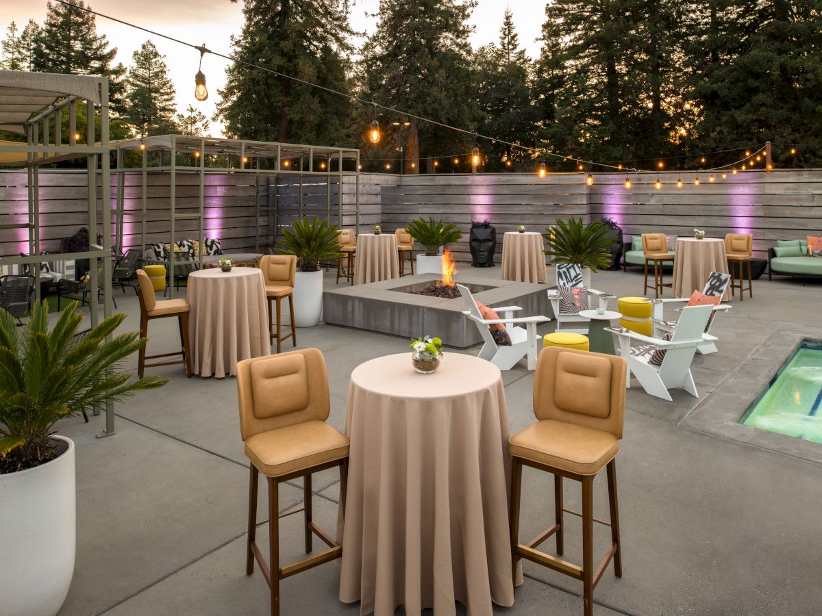 An outdoor patio setup with tables, chairs, string lights, potted plants, and a small pool, perfect for events and gatherings with a cozy atmosphere.