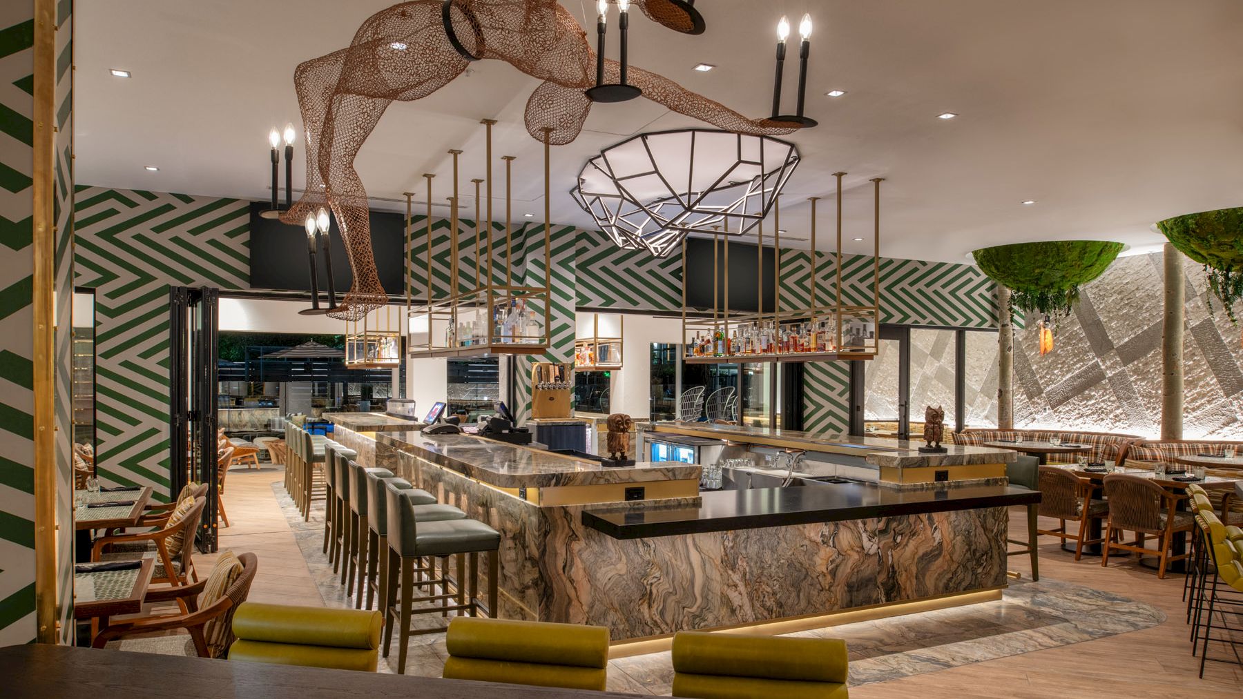 A modern restaurant interior with a central bar, stylish seating, a unique hanging sculpture, and vibrant green and white decor.