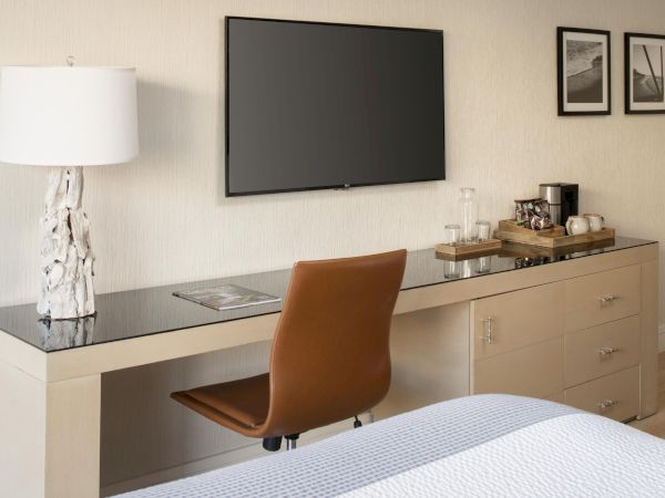 A stylish desk setup features a lamp, chair, TV, framed photos, and a coffee station in a minimalist room.