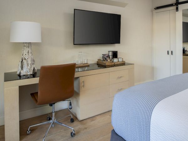 A tidy room with a desk, chair, TV, lamp, wardrobe, and bed with a gray blanket.