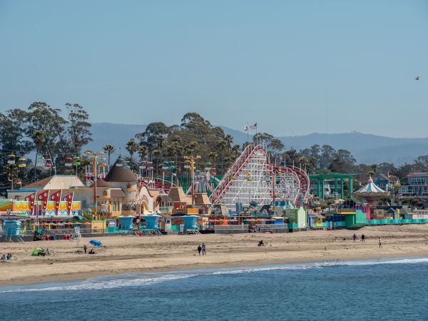 A lively beach scene with an amusement park featuring a variety of rides, including a roller coaster, and colorful buildings in the background.