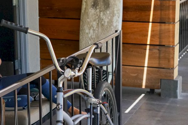 This image shows a bicycle parked next to a surfboard leaning against a wooden partition on a tiled patio.