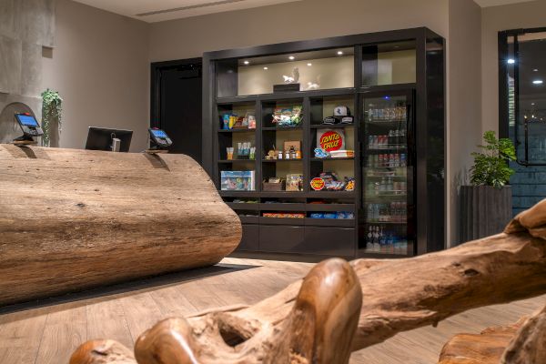 The image shows a wooden reception desk and a snack wall with various food products, beverages, and condiments displayed.