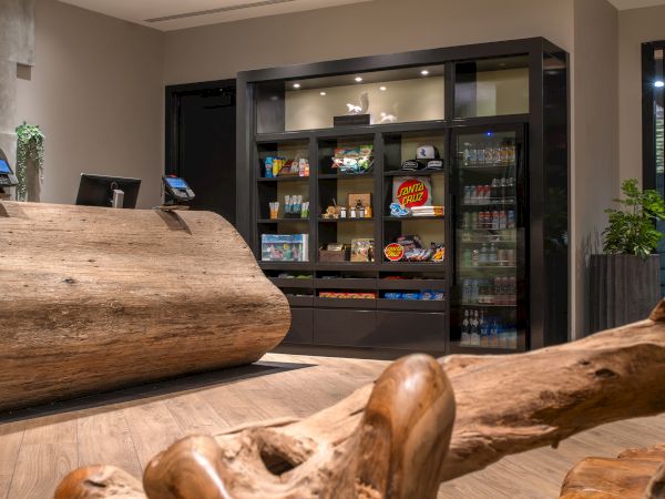 The image shows a wooden reception desk and a snack wall with various food products, beverages, and condiments displayed.