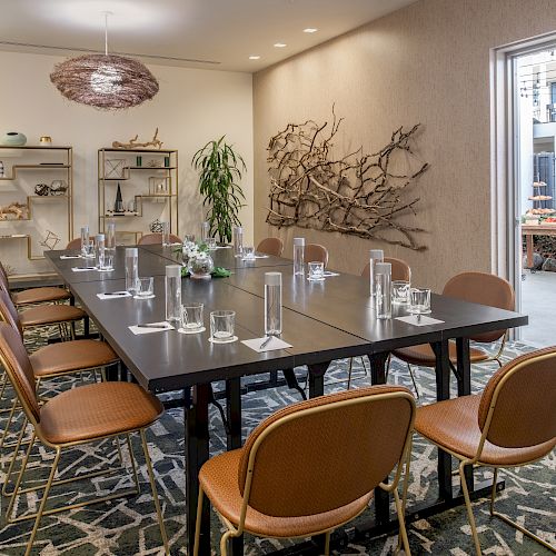 A modern conference room with a long table, chairs, glassware, plants, and decorative items, featuring an open doorway to a patio.