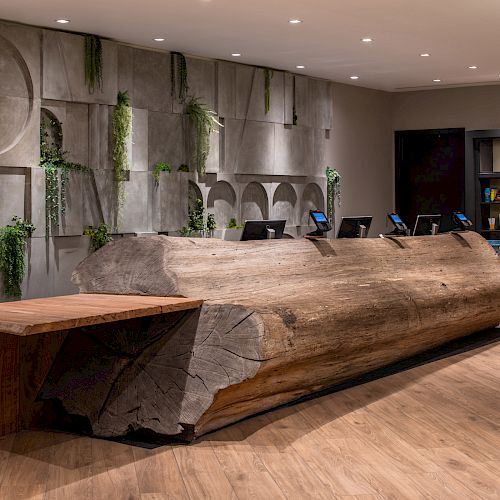 The image shows a modern reception desk made from a large wooden log, with a decorative wall and a small retail shelf in the background.