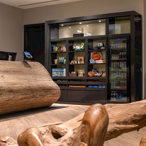 A modern reception area with a wooden desk, shelves displaying various snacks and drinks, and some ornamental plants in the background.