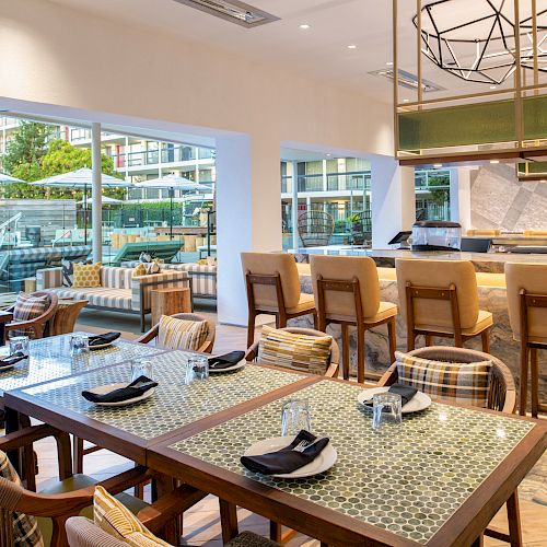 This image shows a modern dining area with tables, chairs, a bar counter, and an outdoor seating area visible through large windows.