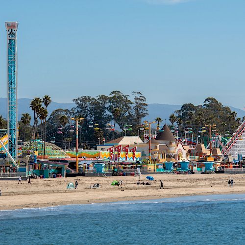 An amusement park with rides and attractions is located by the beach, featuring a roller coaster and a tall tower ride.