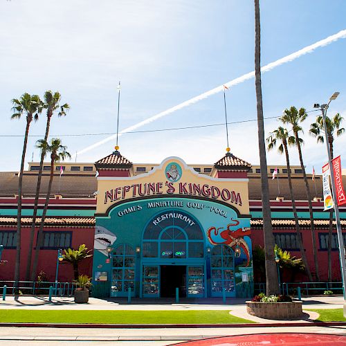 The image shows the entrance to Neptune's Kingdom, a seaside-themed amusement area with palm trees and a clear sky in the background.