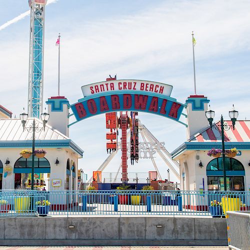 Entrance to Santa Cruz Beach Boardwalk with colorful signs, ticket booths, and amusement rides visible in the background, under a clear sky.