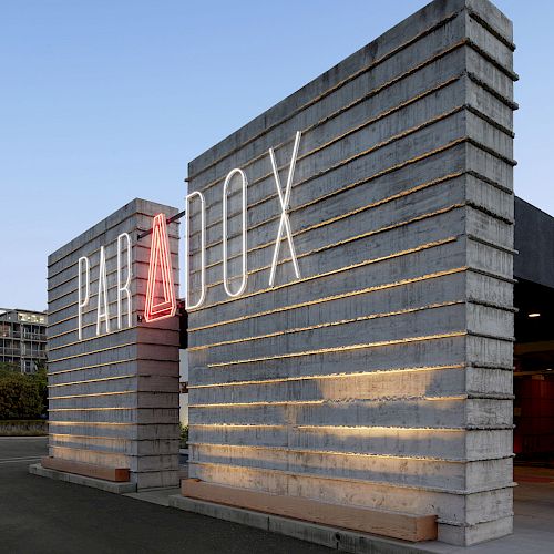 This image shows a modern, industrial-style building entrance with the word "PARADOX" displayed prominently on it.