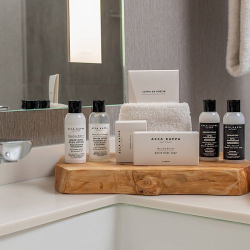 A bathroom counter with grooming products and towels arranged neatly on a wooden tray next to a sink and faucet, against a mirror.