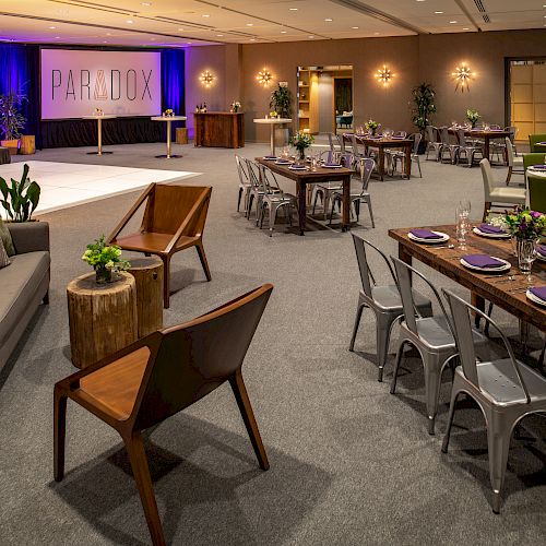 A modern event space with various seating arrangements, including tables and a couch, and a stage with 