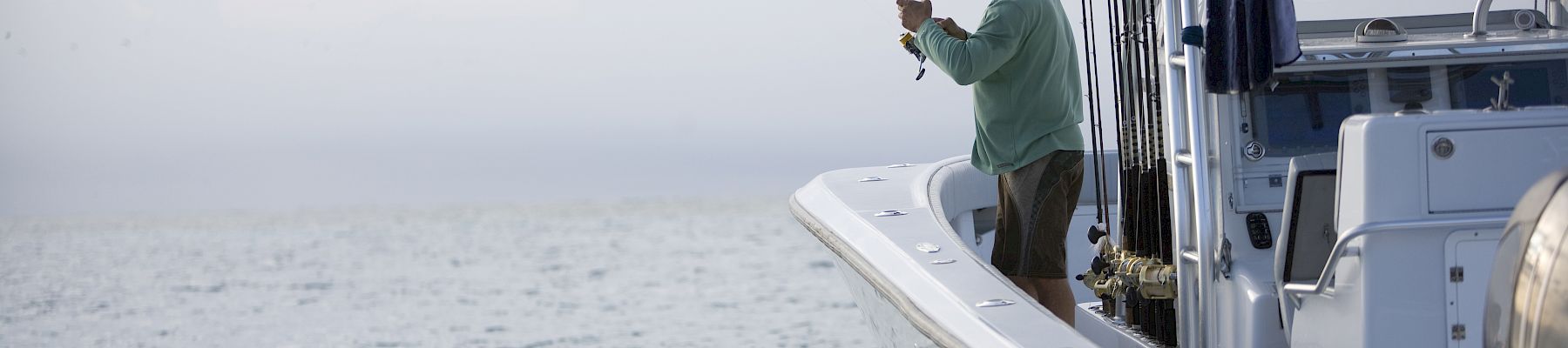 A person on a boat is fishing, bending the rod with the ocean in the background, overcast sky, calm water.