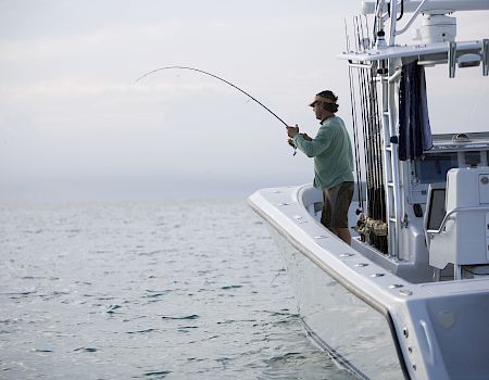 A person on a boat is fishing, bending the rod with the ocean in the background, overcast sky, calm water.