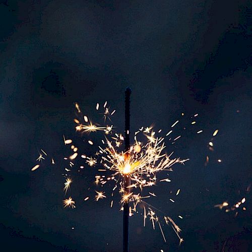 A lit sparkler emitting bright sparks against a dark background.