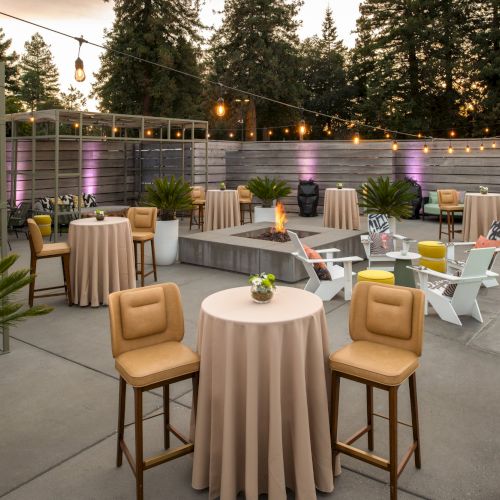 The image showcases an outdoor event area with round tables, upholstered chairs, string lights, a small pool, and surrounding trees.