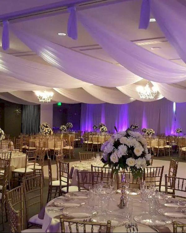 The image shows an elegantly decorated banquet hall with draped ceilings, floral centerpieces, chandeliers, and purple accent lighting.