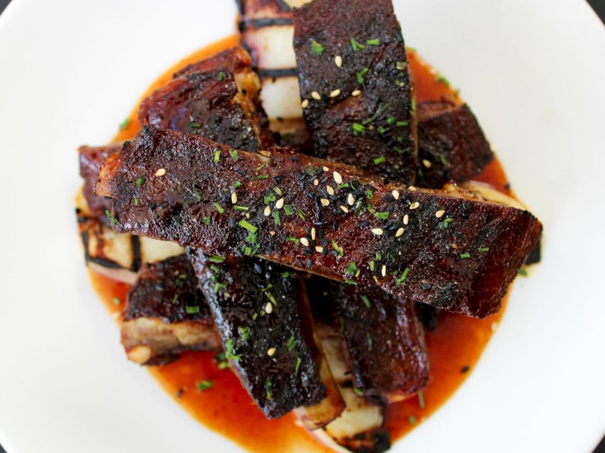 A plate of barbecued pork ribs garnished with herbs, served on a white plate with sauce.