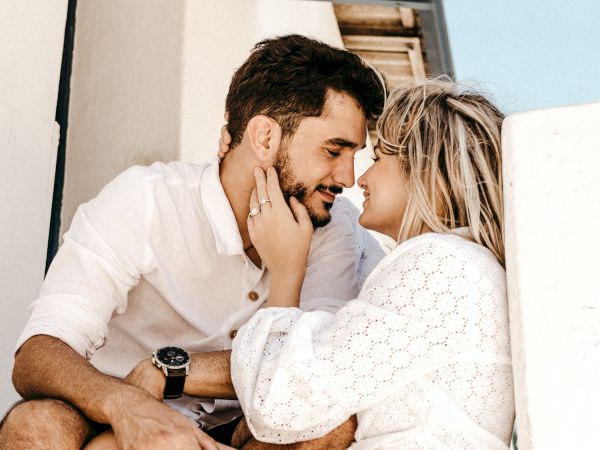 A couple sits closely together, looking into each other's eyes with affectionate smiles. One person gently touches the other's face.