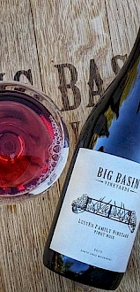 A bottle of Big Basin Vineyards wine and a glass of red wine on a wooden surface.