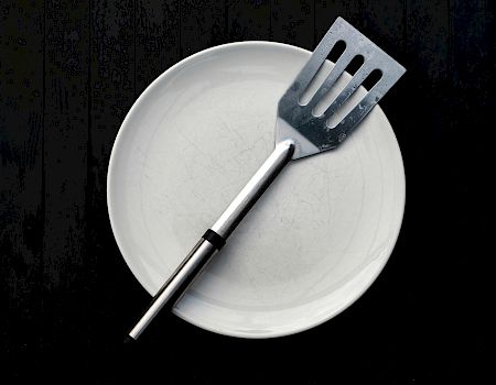 A white plate with a spatula resting across it on a dark surface. Ending the sentence.