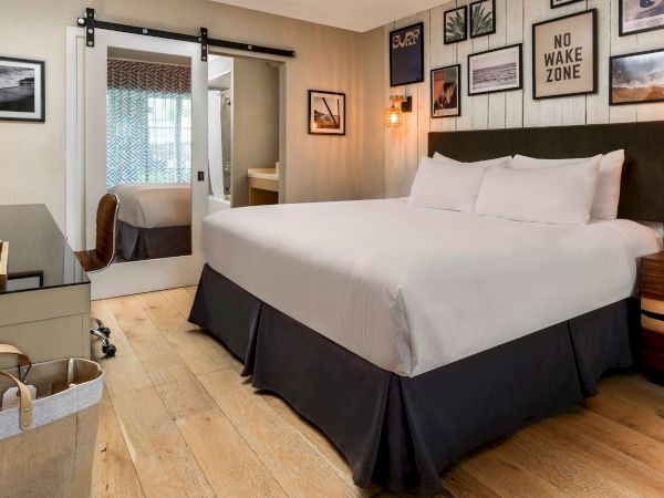 Cozy hotel room with a large bed, bedside lamps, and beachy wall art, including a &ldquo;NO WAKE ZONE&rdquo; sign.