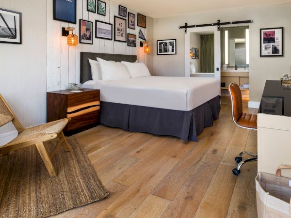 A cozy hotel room with a large bed, framed wall art, lamps, and a small bar area in the corner.