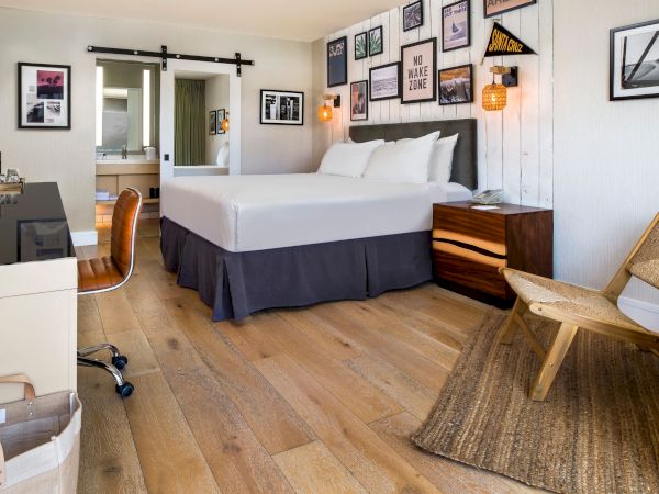 A cozy hotel bedroom with a king bed, nightstands, desk with minibar, woven chair, and beach-themed wall art.