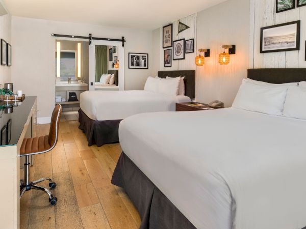 Modern hotel room with two neatly made beds, framed wall art, warm lamps, and a small vanity area.