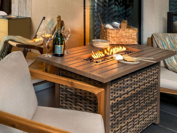 Cozy patio scene with a tabletop grill/fire, skewers and plates of food, plus wine and glasses toasting by the flames.