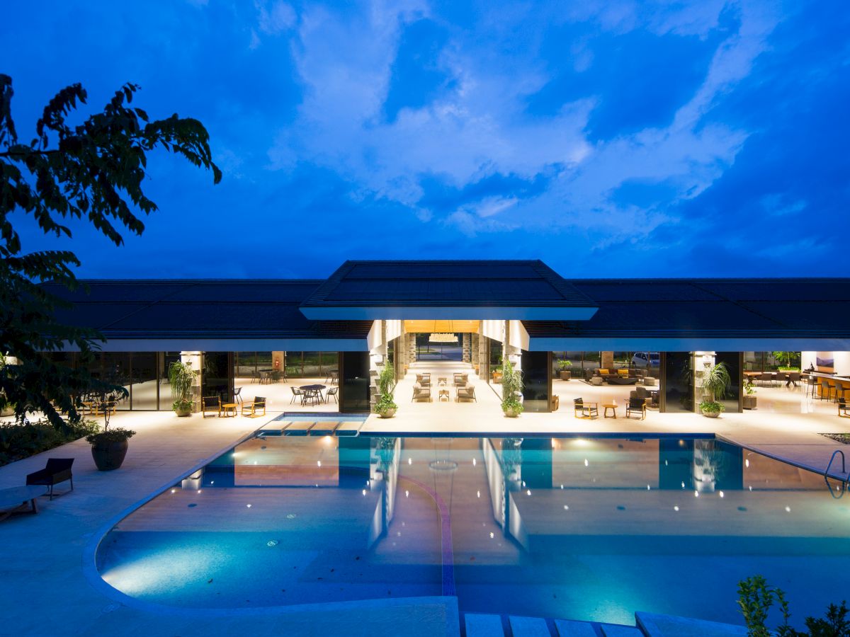 This image features a luxurious outdoor swimming pool area at night, with a modern, well-lit building in the background.