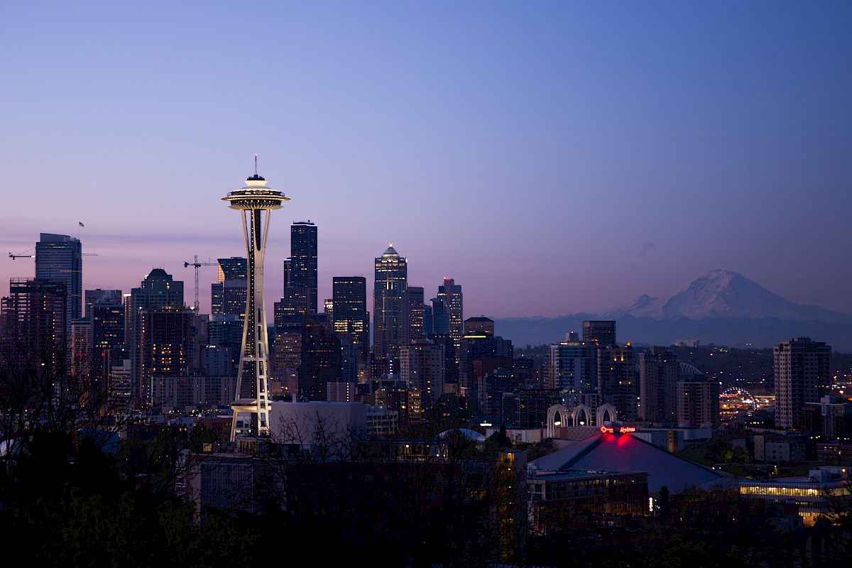 This image depicts the Seattle skyline at dusk, featuring the iconic Space Needle and Mount Rainier in the background.