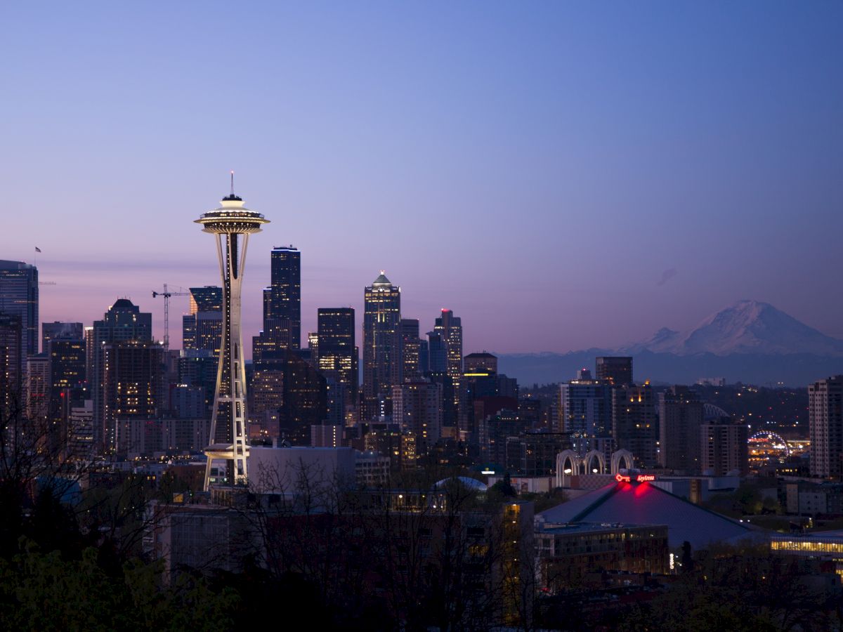 This image depicts the Seattle skyline at dusk, featuring the iconic Space Needle and Mount Rainier in the background.