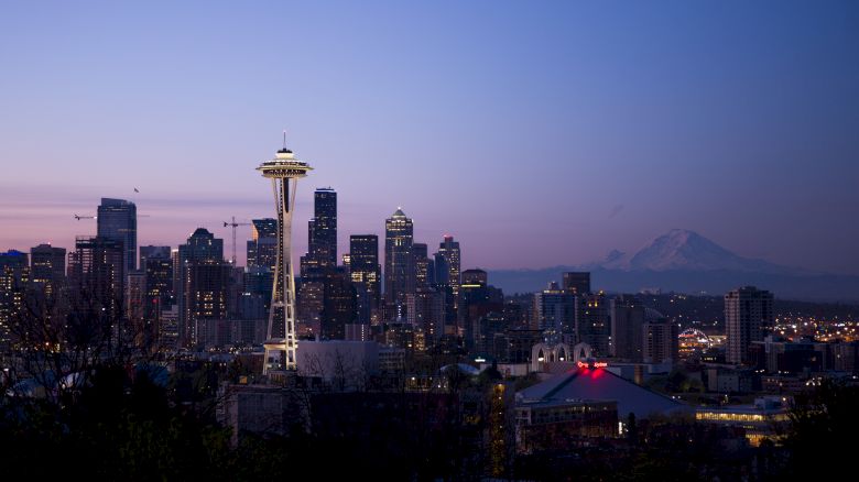 This image depicts the Seattle skyline at dusk, featuring the iconic Space Needle and Mount Rainier in the background.